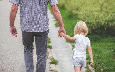 a dad holding his young daughters hand while walking along a street