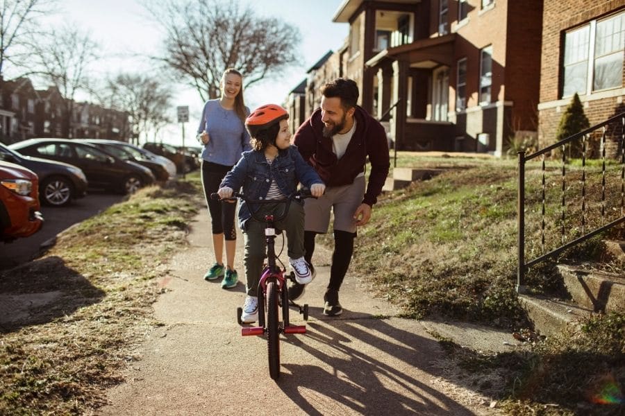 a mother and father teaching their child to ride a bike down the sidewalk