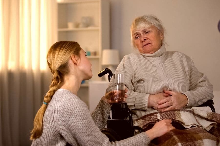a young woman trying to persuade her elderly relative to drink a glass of water