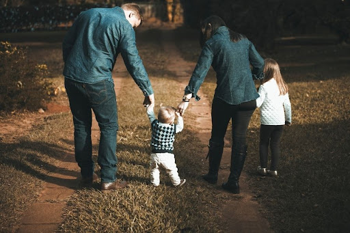 a mother and father walking in the park with their two young children