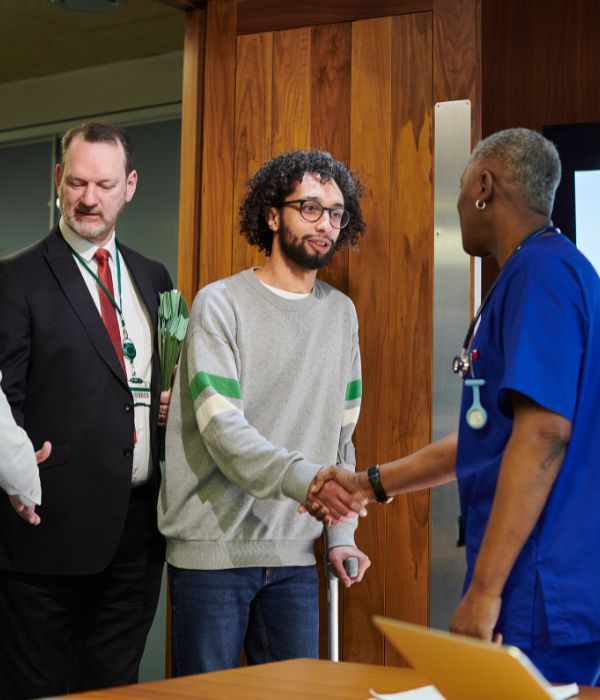 An walking with a cane, shaking the hand of a doctor. His personal injury lawyer stands beside him.