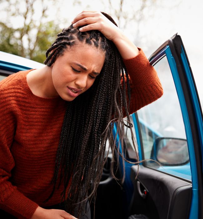a woman stepping out of a car after an auto accident, holding her injured head